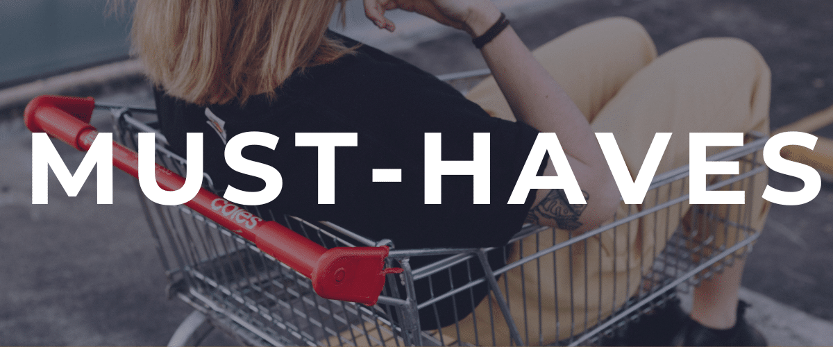 A person sits in a shopping cart outdoors, wearing beige pants and a black shirt, with Pop Culture Picks and MUST-HAVES in large white text across the image.