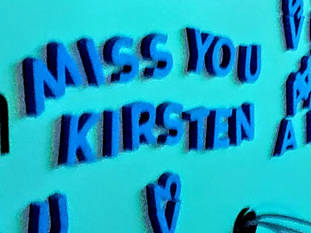 Blue letters on a turquoise wall spell out MISS YOU KIRSTEN, evoking the vibrant energy of EDC. Other scattered blue letters and shapes dance around the main message.